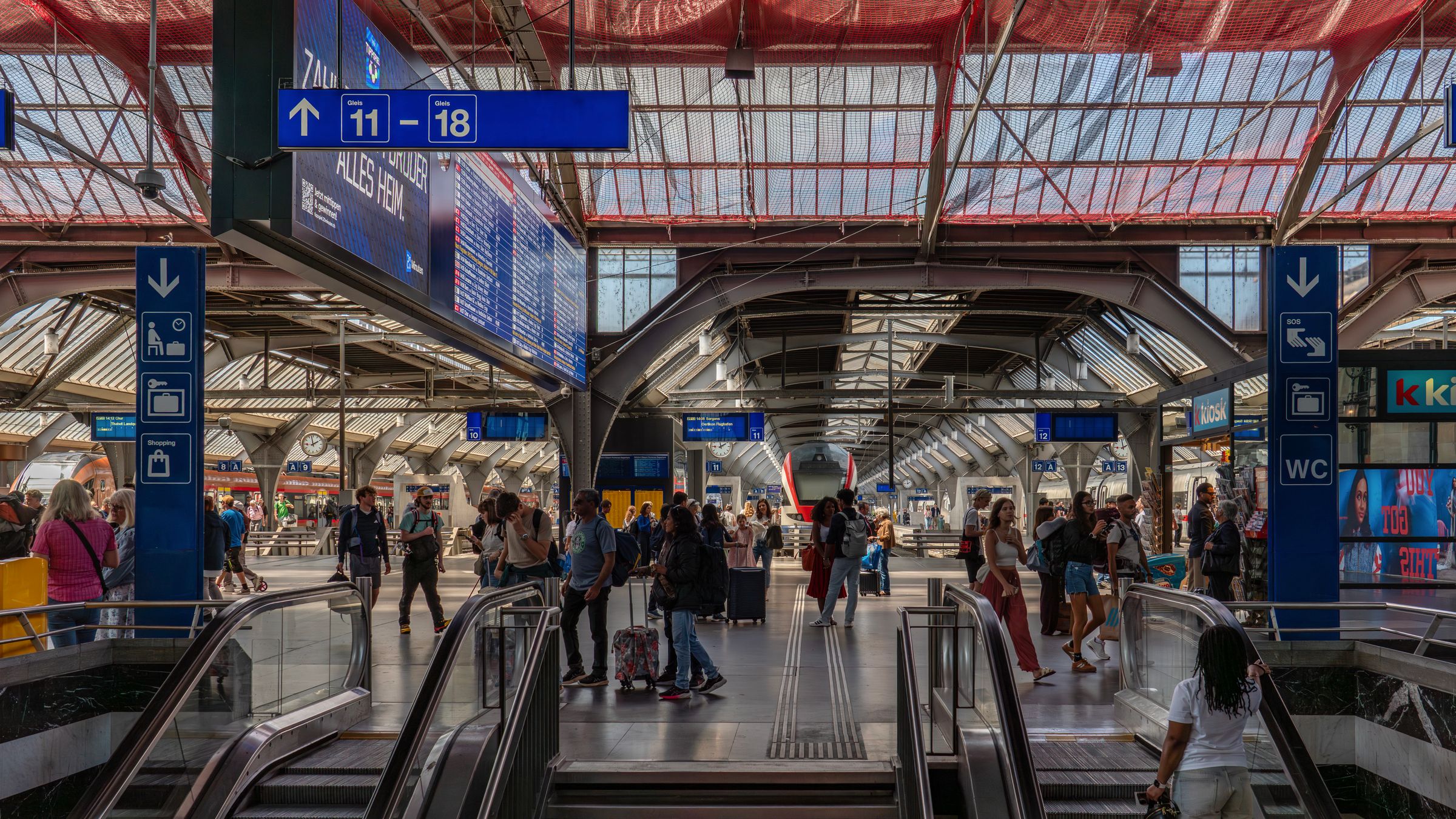 Commuters spread across a wide station hall with departure boards and a long clear span above.